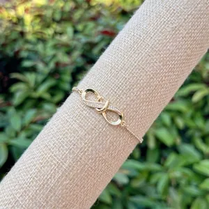 18K gold plated infinity bracelet featuring clear zircon stones on a linen display stand
