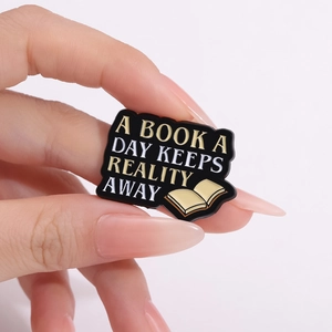Enamel book brooch with text A BOOK A DAY KEEPS REALITY AWAY on black background