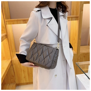 Detail of grey quilted shoulder bag with chain strap worn by model in a stylish setting