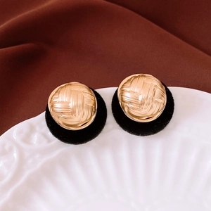 Close-up of golden vintage round button earrings with woven texture on a white ceramic plate