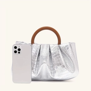 Detail of silver crocodile-textured evening bag with a brown round handle and phone scale