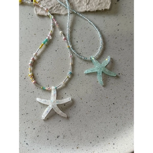 Detail of starfish pendant necklaces with colorful rainbow beads on a ceramic plate