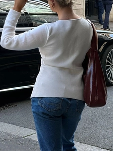 Back view of a woman wearing a white knit sweater with a dark red leather shoulder bag