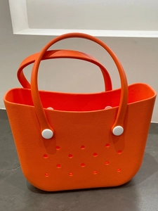 Close-up of bright orange EVA beach bag showing circular holes and white attachment buckles