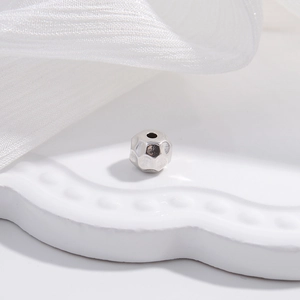 Detailed macro view of S925 silver irregular faceted spacer bead on a white ceramic plate