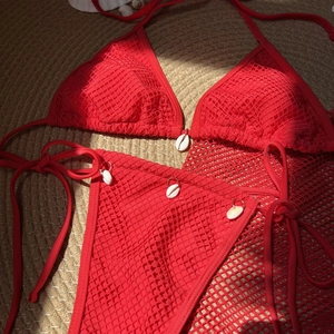 Detail of red mesh bikini set with natural white seashells on woven straw mat background