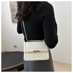 Detail of white quilted crossbody bag with gold chain strap and metal buckle on shoulder