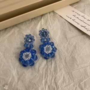 Detailed view of handcrafted Klein blue beaded flower earrings on textured background