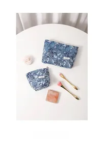 Detailed view of blue paisley cosmetic bag set with zipper and brand label on white stand
