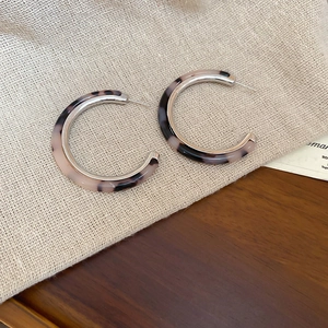 Detailed view of silver C-shaped earrings with tortoiseshell resin on a textured surface