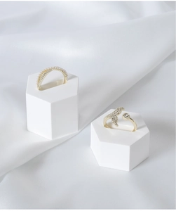 Detail of gold pearl and fishtail rings on white hexagonal display stands with satin