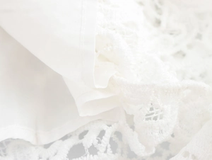 Gros plan détaillé montrant la dentelle blanche française et le tissu lisse sur la robe