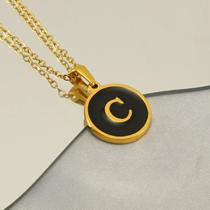 Detailed macro view of the gold round pendant with a black enamel letter C on the chain