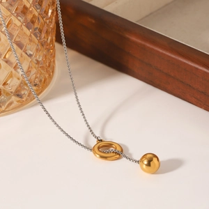 Minimalist silver chain necklace with gold ring and ball pendant on a white marble surface