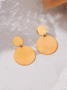 Gros plan sur des boucles d'oreilles cercles dorées en acier sur fond de marbre blanc