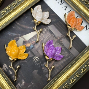 Detailed view of four colorful enamel magnolia brooches in a vintage gold frame