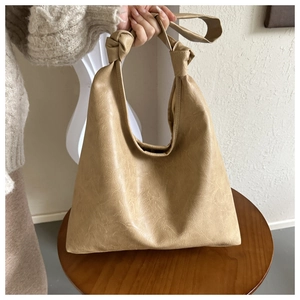 Close-up of beige textured leather hobo bag with unique knotted strap detail on a stool