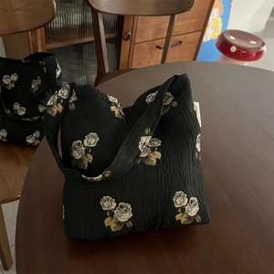 Detail of black textured fabric shoulder bag featuring vintage white rose floral patterns