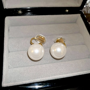 Detail shot of golden clip-on earrings with large white pearls on grey velvet lining