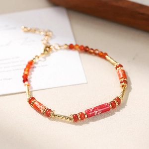 Macro shot of colorful beaded bracelet with red textured tubes and golden metal accents