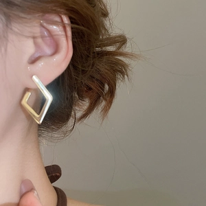 Detailed view of modern geometric golden diamond hoop earrings worn by a female model