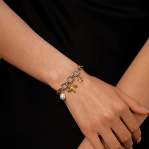 Detailed view of bicolor chain bracelet with starfish charm and white pearl on wrist