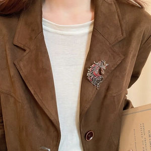 Detailed view of a vintage silver horse brooch with red rhinestones on a brown suede blazer