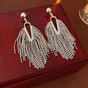 Macro shot of silver metal tassel earrings with intricate bead strands on vintage wood