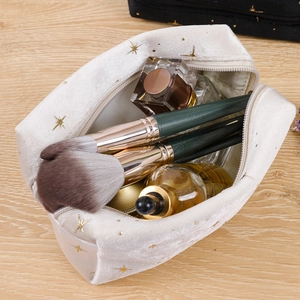 Overhead view of off-white velvet cosmetic bag with gold stars holding brushes and perfume