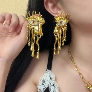 Macro detail of oversized gold evil eye earrings with liquid metal design and rhinestones