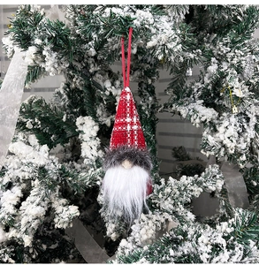 Detail of a red plaid gnome ornament hanging on a snow-covered Christmas tree branch
