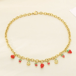 Collier en or avec pendentifs fraise rouge et citron sur fond beige texturé