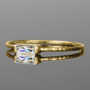 Detail of gold hammered ring with rectangular baguette cut clear gemstone on mirror surface