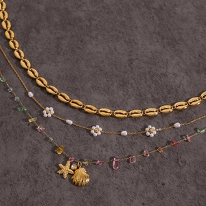 Detail of layered gold necklaces with sea shells, flowers and colorful beads on dark background