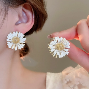 Detail view of handmade raffia daisy earrings with gold center worn by a model