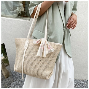 Detail of straw tote bag with floral embroidery and white leather straps on a model