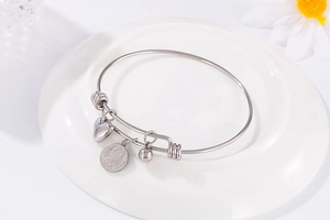 Detail of adjustable stainless steel bangle with heart, bead, and coin pendants