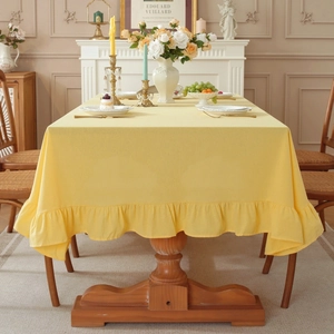 Elegant solid yellow cotton linen tablecloth with ruffled edges on a wooden table