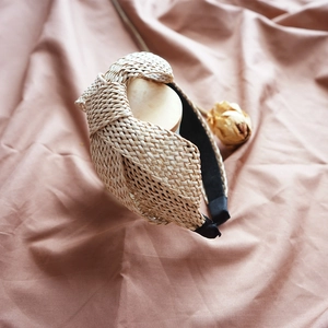 Close-up of beige raffia knotted headband with straw texture on pink silk fabric