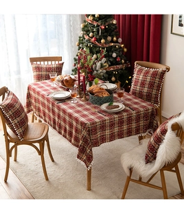 Close-up of red plaid Christmas table runner and chair cushion with white pom pom trim