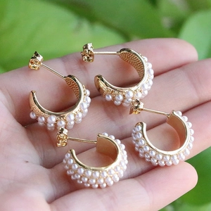 Elegant C-shaped gold-plated earrings with three rows of white pearls held in hand
