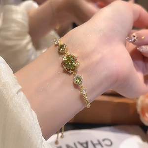 Detailed macro view of 18k gold plated bracelet with emerald green zircon stones on wrist