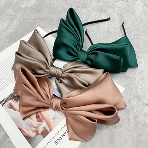 Three-layered satin bow headbands in dark green and bronze on a stylish cement surface