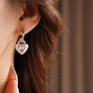 Close-up of heart-shaped silver earrings with pink gemstones worn by a model