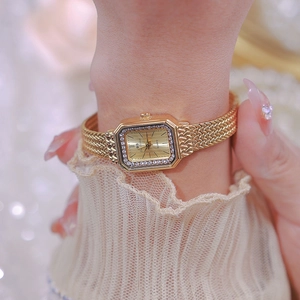 Close-up of a gold rectangular watch with diamond bezel and woven mesh bracelet