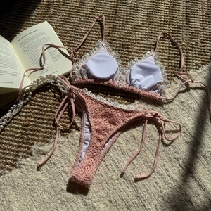 Flat lay of a pink lace bikini set with crochet texture and ribbon ties on a cozy rug