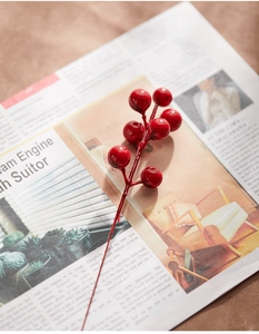 Close-up of artificial red holly berry stems on a vintage newspaper for Christmas decor