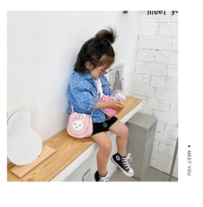 Pink rabbit-shaped kids crossbody bag with 3D ears and bow shown in a lifestyle setting