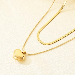 Close-up of golden double-layer necklace featuring a sleek heart pendant and snake chain