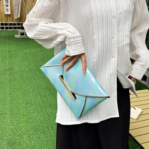 Close-up of holographic envelope clutch bag with metal trim held against natural background